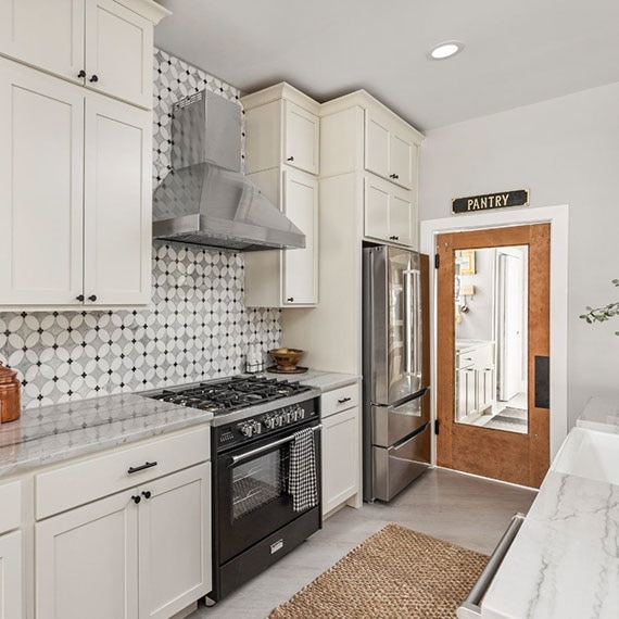 Renovated kitchen with gray natural quartzite countertops, black mirror and white & gray marble petal mosaic backsplash, white cabinets, and stainless steel appliances.