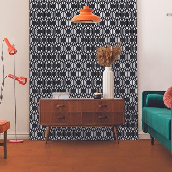 Eclectic style room with retro wood side table in front of black & white hexagon wall tile, orange concrete look tile floor, and green velvet loveseat with coral throw pillow.